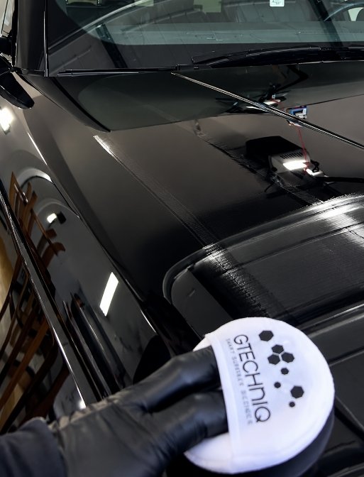 Hand applying ceramic coating paint protection to black car hood