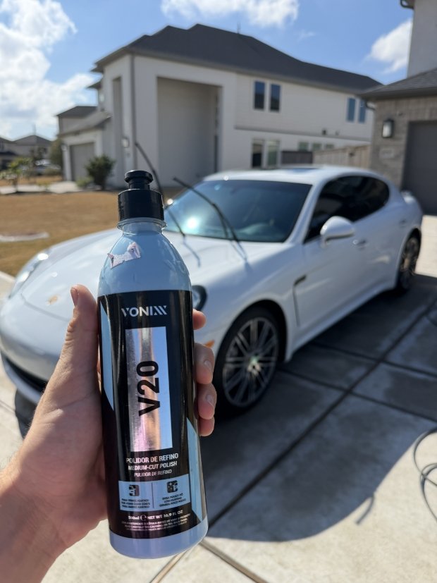 Holding Vonixx V20 medium cut polish bottle in front of white Porsche